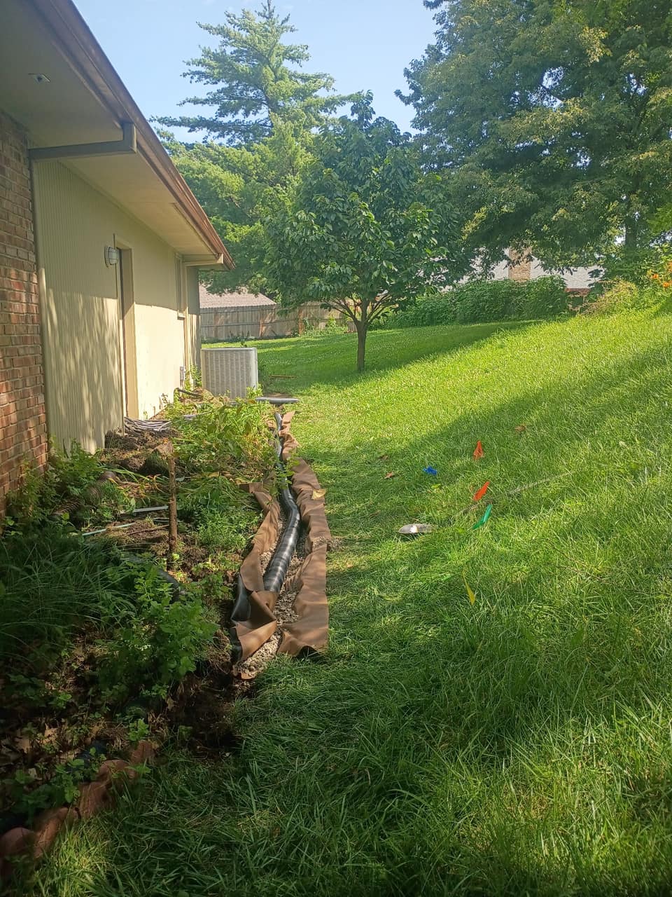 Drain line trench running the length of the foundation down a sloped lawn