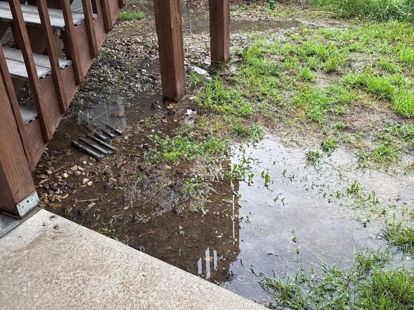 Standing rainwater pooled against a house foundation beside deck stairs