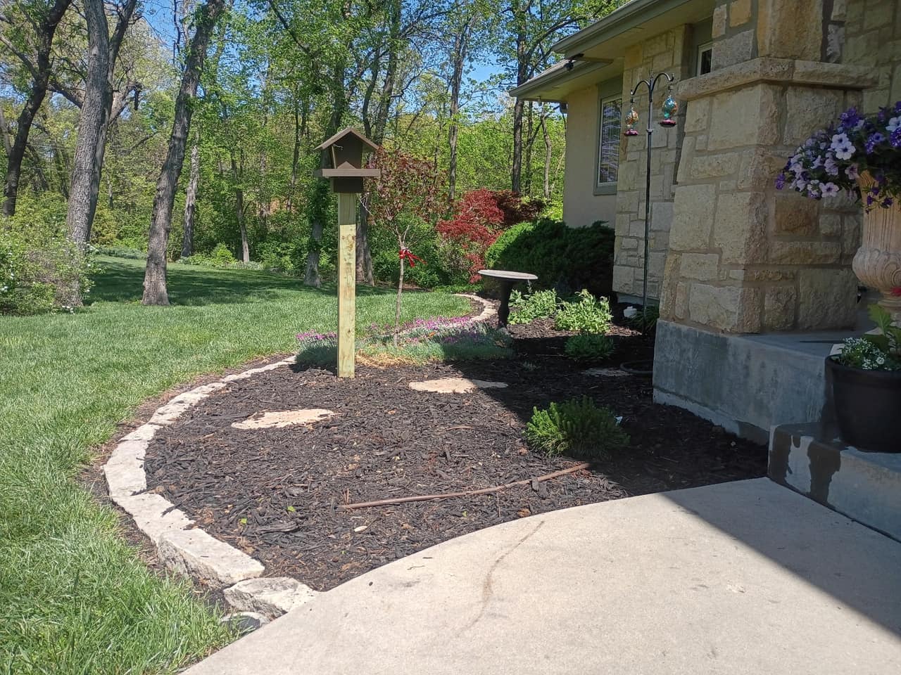 Curved stone-edged bed with fresh dark mulch following a walkway to a house entry