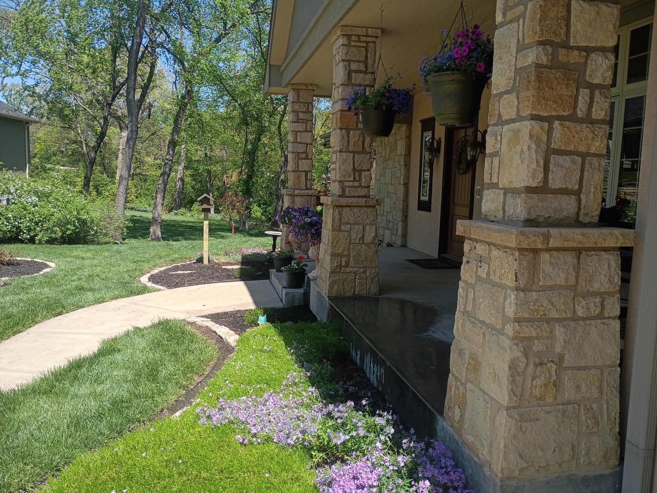 Stone-edged bed in flower beside a covered porch and walkway